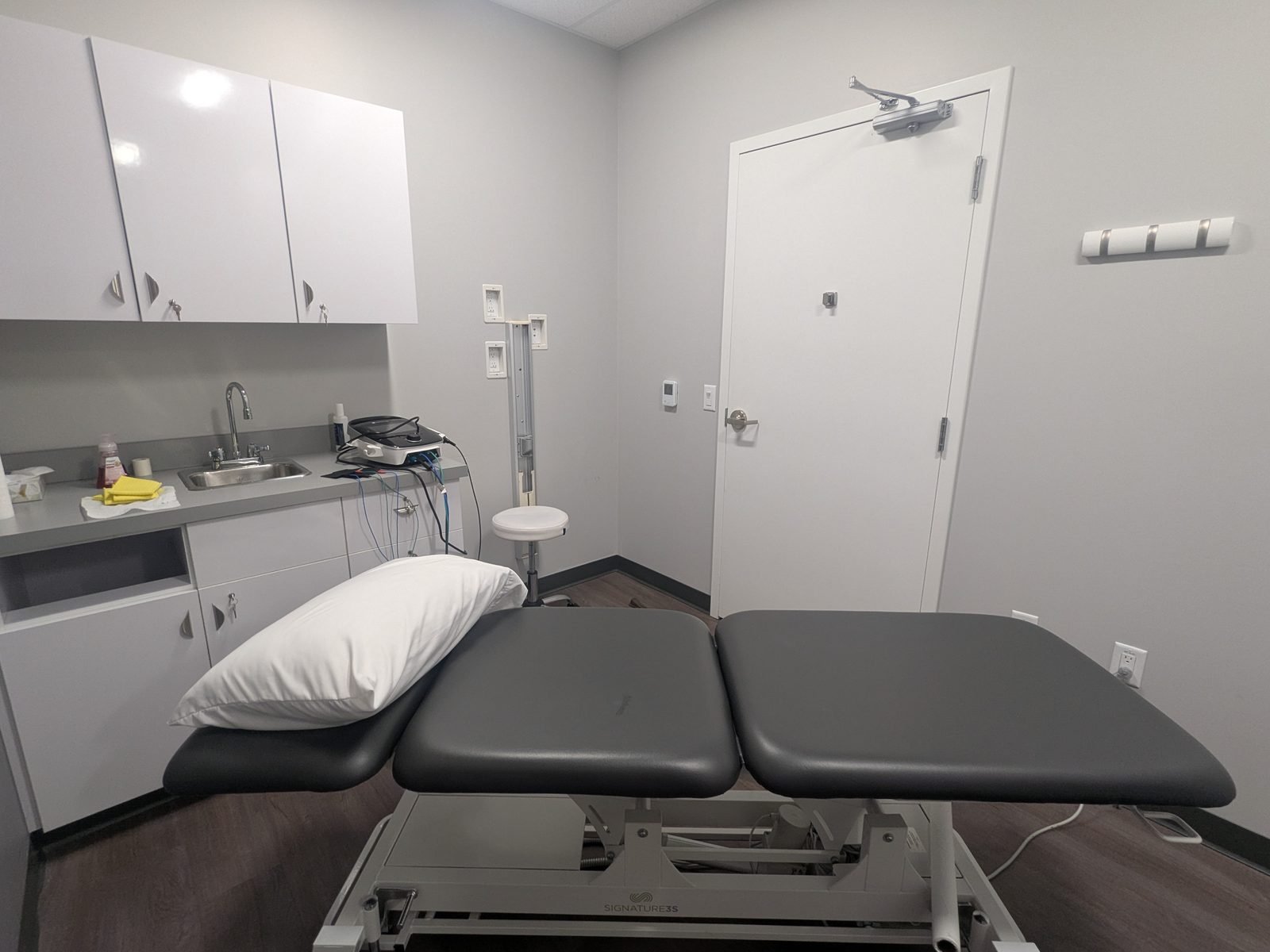 A treatment room with a powered plinth, sink and cabinets