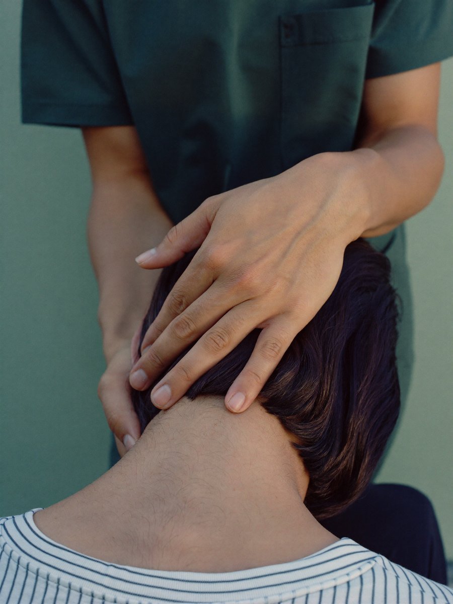 A physiotherapist working with both hands on a seated patient's neck and shoulders