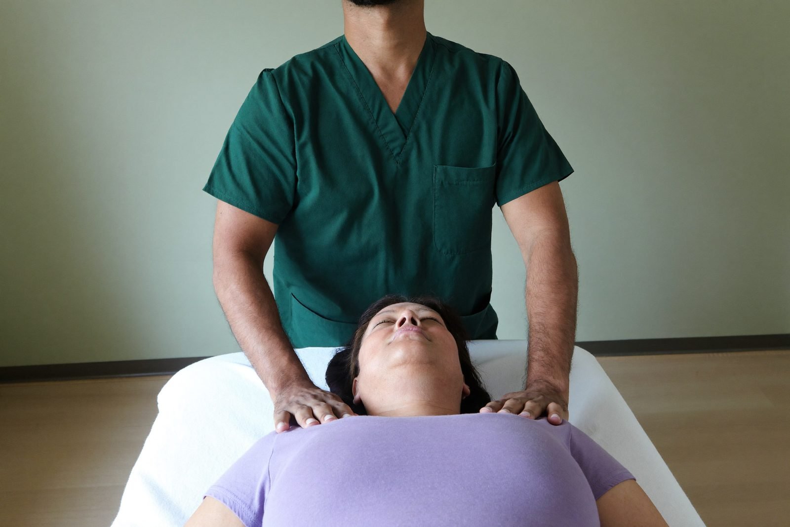 A therapist using flat, relaxed hands and very light contact at the base of a patient's neck