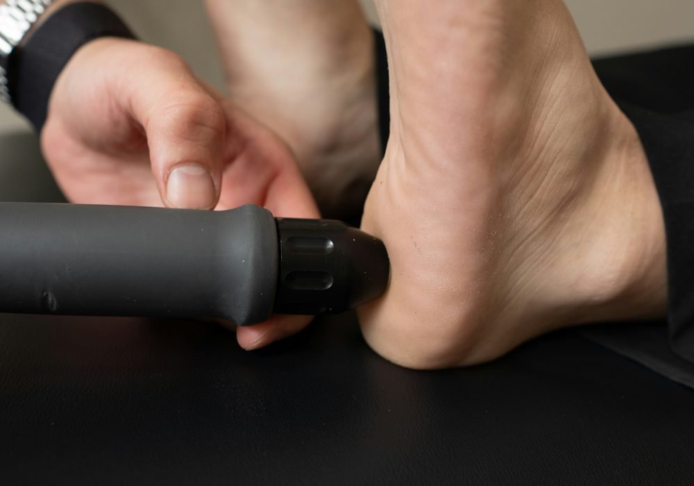 A clinician treating the back of a patient's heel with a handheld therapy device